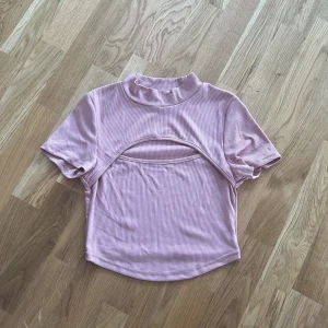 Rosa randig topp - Säljer en söt rosa randig topp med korta ärmar och en unik design med öppning framtill. Perfekt för en trendig look.