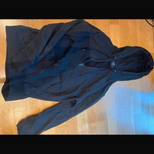 Svart huvjacka från H&M - Säljer en svart huvjacka från H&M i storlek XS. Jackan har dragkedja framtill och en mysig huva med snörning. Perfekt för en avslappnad stil.