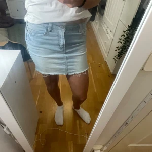 Ljusblå jeanskjol - Snygg ljusblå jeanskjol med fransig nederkant och klassisk femficksdesign. Perfekt för en avslappnad stil. Kjolen har en knapp och dragkedja framtill.