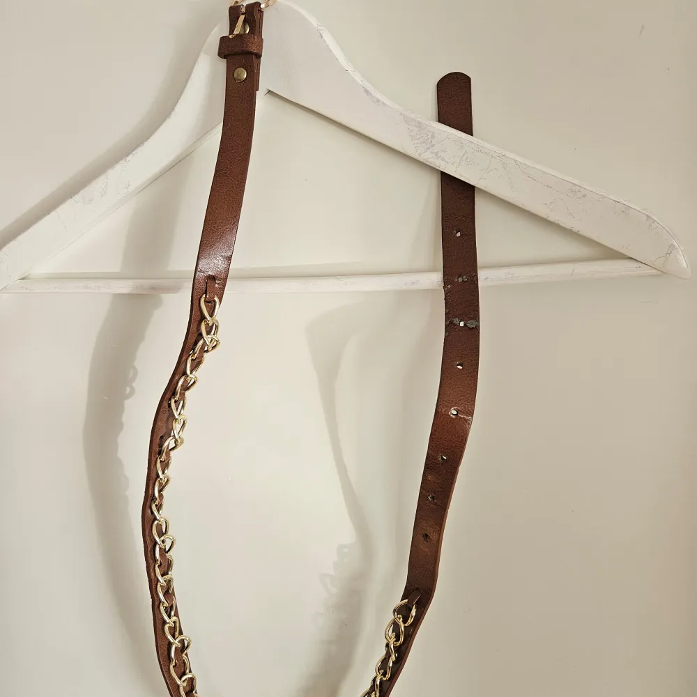Snyggt brunt bälte med guldkedja som detalj. Perfekt för att ge en extra touch till din outfit. Justerbar längd med flera hål för perfekt passform.. Asusteet.