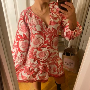 Rosa och vit blommig klänning - Säljer en söt klänning med rosa och vitt blommönster. Den har en v-ringad hals och långa ärmar. Perfekt för en somrig look! Aldrig använts!