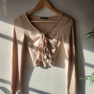 Beige ribbad topp från FB Sister - Säljer en beige ribbad topp från FB Sister i storlek XS men passar som S. Toppen har långa ärmar och en v-ringad design med knytning framtill. Perfekt för en stilren look.