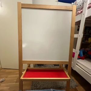 Dubbel-sidig staffli med whiteboard och griffeltavla - Säljer ett praktiskt staffli med en sida som är whiteboard och den andra som är griffeltavla. Perfekt för barnens kreativa stunder! Ramen är i trä och det finns en röd hylla för förvaring av kritor och pennor. Passar bra i barnrummet eller lekrummet. Priset kan diskuteras! 