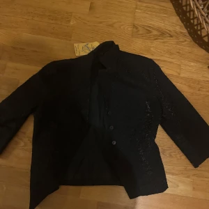 Svart kavaj från Bianca Nygård - Snygg svart kavaj från Bianca Nygård i mycket bra skick. Den har en elegant design med knappar framtill och långa ärmar. Perfekt för både fest och vardag. Passar bra till höst och vår.