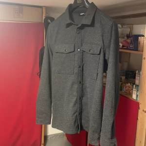 Overshirt Kayoba - Säljer denna helt nya riktigt snygga overshirten då den inte kommer till användning. Riktigt synd att den bara ligger då den passar till allt. Stilren och i topp skick. Passar dig som är mellan 175-190