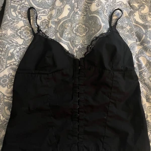 Svart topp - Snygg svart topp från zara 🖤 Knäpps diagonalt på mitten, har spets vid brösten ❤️‍🔥  Funkar både till vardags o festligare tillfällen 🎉 Djur och rökfritt hem.