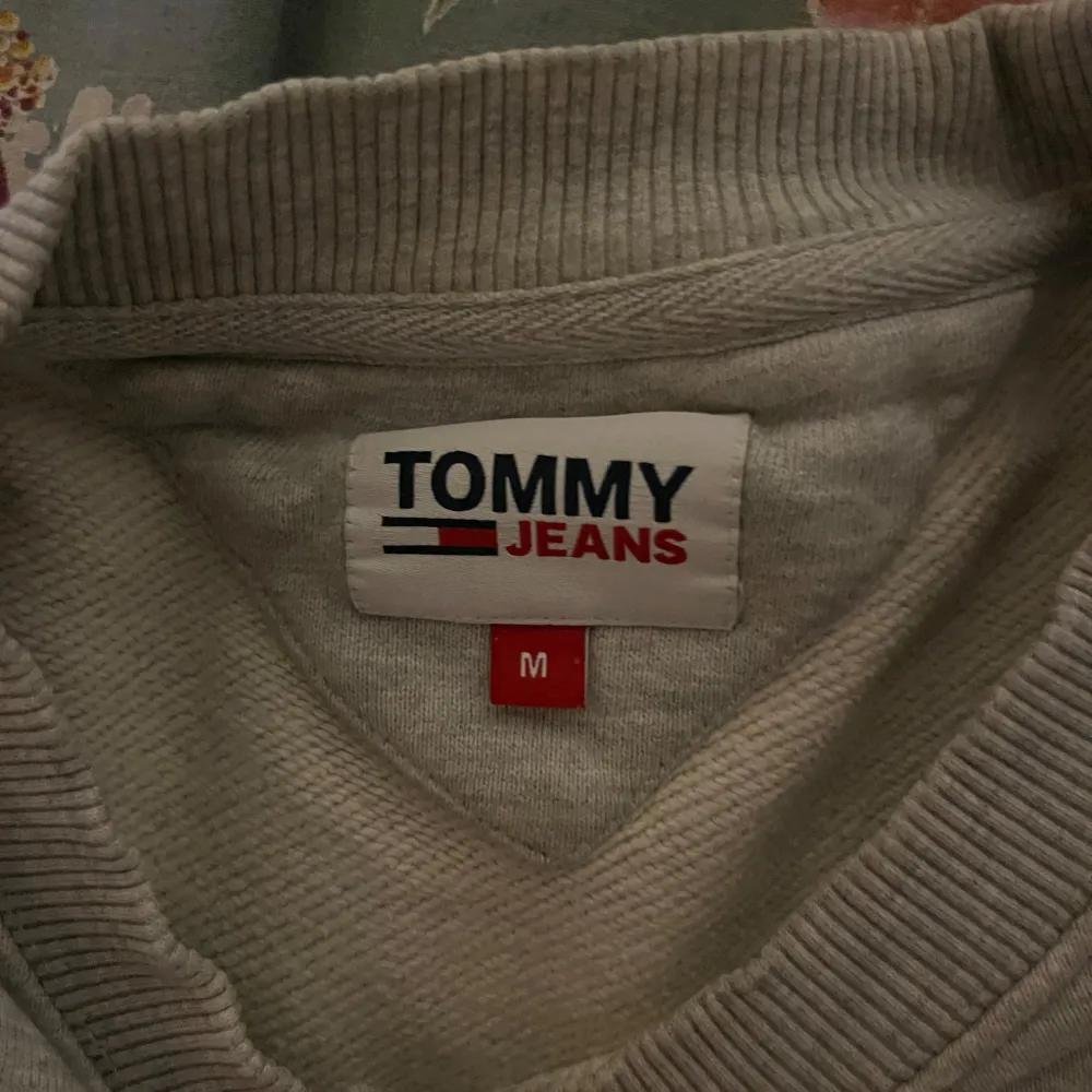 Säljer en stilren grå sweatshirt från Tommy Jeans i storlek M. Tröjan har en klassisk design med ribbade muddar och en liten logga på bröstet. Perfekt för en avslappnad look eller som ett lager under jackan. Passar både höst och vår!. Tröjor & Koftor.