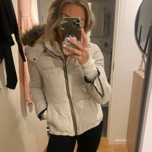 Benvit/ljusbeige vinterjacka - Säljer en benvit/ljusbeige pufferjacka i storlek 36. Jackan har en pälskantad huva och dragkedja framtill. Perfekt för kalla vinterdagar! 🧥❄️