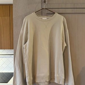 Beige sweatshirt från A Day's March - Storlek L - Säljer en stilren beige sweatshirt från A Day's March i 100% ekologisk bomull. Perfekt för både vardag och chill dagar. Den har en klassisk rund hals och ribbade muddar vid ärmslut och nederkant. Supermjuk och bekväm! Tröjan är i superfint skick, med endast en liten fläck på framsidan som knappt är synlig (se sista bilden).