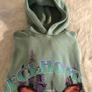 Grön hoodie från BoohooMAN - Säljer en grön hoodie från BoohooMAN i storlek S. Den har ett coolt tryck med ett skelett och fjärilsvingar framför en skog. Perfekt för höst och vår med sin mjuka och bekväma passform. Huvan är fodrad för extra värme. Passar både till vardags och chillkvällar.