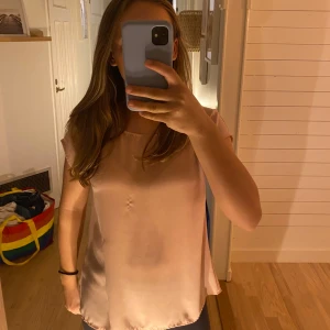 Ljusrosa blus med öppen rygg - Säljer en superfin ljusrosa blus i ett mjukt och glansigt material. Den har en lös passform och korta ärmar, perfekt för både vardag och fest. Detaljen med öppen rygg ger en extra touch av stil. Passar perfekt till jeans eller kjol!