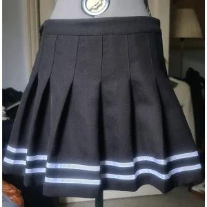 Veckad kjol svart med vita ränder 42 - Nyskick, 100% polyester. Säljer den åt någon annan så notera storleken. Midjevidd: 40, längd: 40.