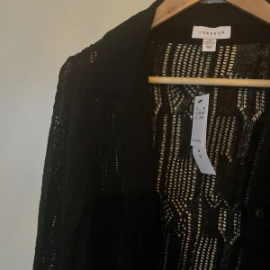 Skjorta/kofta i bomull strl M - Svart stickad skjorta/kofta sydd i ett genomskinligt mönster från Topshop, strl M. Aldrig använd med etiketter kvar. Nypris 569.  