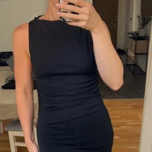 Svart ärmlös klänning - Säljer en elegant svart ärmlös klänning i tight passform. Perfekt för festliga tillfällen. Klänningen är i mycket bra skick och har en stilren design som framhäver figuren.