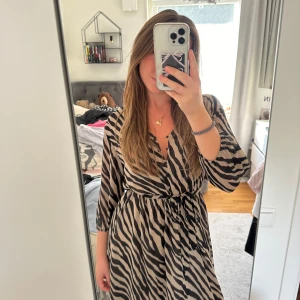 Zebramönstrad omlottklänning - Säljer en superfin zebramönstrad klänning med trekvartsärm. Klänningen har ett knytband i midjan och går ner till mitten på vaden ungefär💞