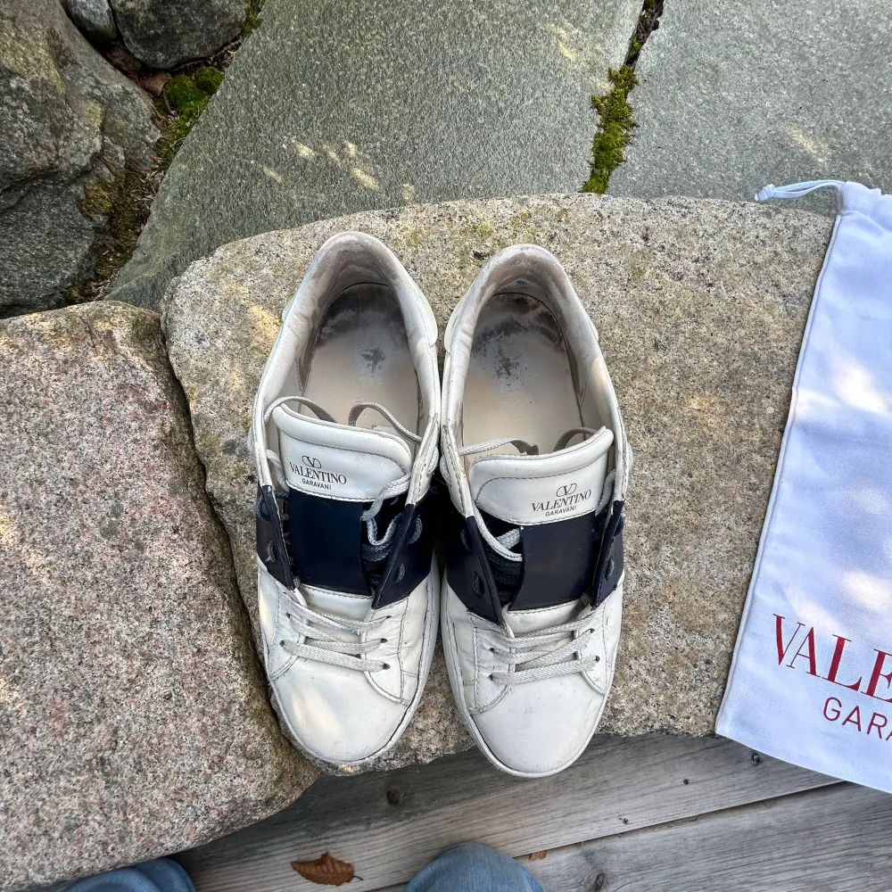 Säljer ett par vita Valentino Garavani sneakers med marinblåa detaljer. Skorna har en klassisk design.De är lite smutsiga men går och göra rent. Skick 6/10. Skorna är storlek 40 men passar även 41-41,5. Pris går och diskutera vid snabb affär.. Skor.