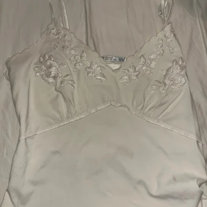 Vit linne med broderade blommor - Säljer ett superfint vitt linne med tunna axelband och vackra broderade blommor på framsidan. Perfekt för sommardagar eller som ett sött lager under en kofta. Linnet är i bra skick och har en romantisk stil.