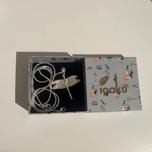 Ioaku trollslända 💕 - Säljer mitt silvriga Ioaku halsband med en trollslända som berlock. Säljer då jag ska byta till guld och ej fått användning för det. Använd ca 2 gånger så är i nyskick, köpt för 499kr. Både den långa och korta kedjan ingår!🥰