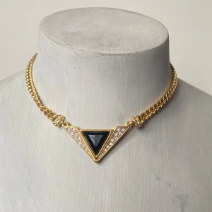Guldhalsband med triangulär svart sten - Säljer ett elegant vintage guldhalsband med en cool triangulär svart sten i mitten. Halsbandet har en kedja i guld och är dekorerat med små glittrande stenar runt den svarta triangeln. Perfekt för att ge en lyxig touch till vilken outfit som helst!