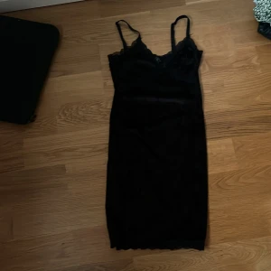 Svart klänning från H&M Divided - Säljer en elegant svart klänning från H&M Divided. Den är ärmlös med smala axelband och har vackra spetsdetaljer vid halsringningen. Perfekt för en festlig kväll eller en utekväll med vänner. Klänningen är i nyskick och redo att bäras!