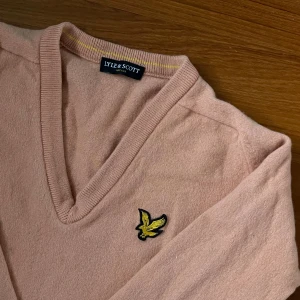 Beige tröja från Lyle & Scott - Säljer en superfin beige rosa tröja från Lyle & Scott. Den har en snygg v-ringning och deras klassiska logga på bröstet. Perfekt för både höst och vår! Tröjan är i ok och är riktigt skön att ha på sig. Lite fläckig