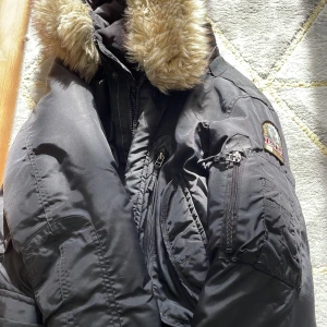 Parajumper jacka - Säljer en svart vinterjacka från Jackets Industry. Den har en mysig pälskrage och är perfekt för kalla dagar. Jackan har en dragkedja och flera praktiska fickor. Den är i bra skick och redo för en ny ägare!