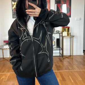 Svart hoodie med mönster - Säljer en svart hoodie med coola mönster i vitt. Den har en dragkedja framtill och en stor huva. Perfekt för en avslappnad stil och passar bra till jeans. Den är långärmad och har en bekväm passform.