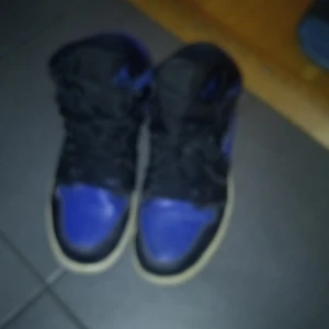 Svart och blå Nike Air Jordans - Snygga Nike Air Jordans i svart och blått med klassisk hög design. Skorna har snörning och en kontrasterande vit sula som ger en cool look.