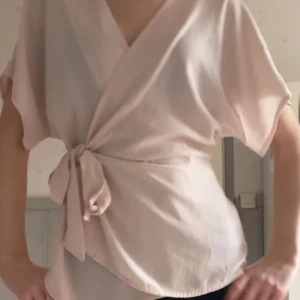 Rosa omlottopp - Säljer en stilren rosa omlottopp med knytband i midjan💕 Toppen har korta ärmar och en v-ringad design som ger en elegant look💕storlek 40 men passar mig med 34-38