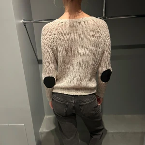 Beige stickad tröja med svarta detaljer - Säljer en beige stickad tröja med svarta armbågslappar. Tröjan har en avslappnad passform och långa ärmar, perfekt för kyligare dagar. Den är både stilren och bekväm, ett måste i garderoben!