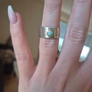 Handgjorda silverring m. turkos sten - Elegant silverring av känd svensk formgivare med en rund turkos sten i mitten. Ringen har en bred design och kommer i en vacker blommig tygask. Värderad av auktionshus till 1000:-. Aldrig använd men kan behövas putsas upp lite