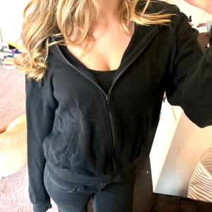 Svart zip-up hoodie  - Säljer en svart huvtröja från Cubus med dragkedja och fickor framtill. I storlek S. Tröjan har en klassisk design med huva och långa ärmar. Perfekt för en avslappnad stil. Tröjan har ett pyttelitet håll på framsidan (kolla bild) men inget man ser vid användning, och även få trådar vid ärmen ( kolla bild) förutom det är tröjan i bra skick. 