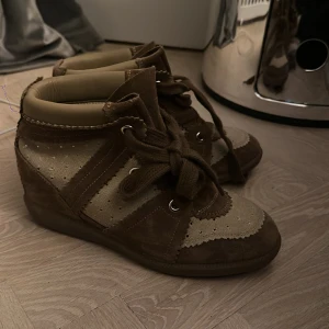 Bruna sneakers med snörning - Snygga bruna sneakers med snörning och detaljer i mocka och syntet. Skorna har en högre modell med vadderad kant för extra komfort. Perfekta för en avslappnad stil.