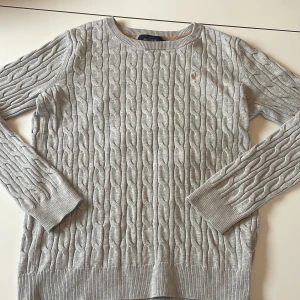 Grå stickad tröja från Morris - Snygg grå stickad tröja från Morris med kabelstickat mönster. Tröjan har långa ärmar och en rund halsringning. Perfekt för kyligare dagar och ger en stilren look.