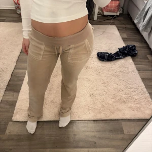 Beige mjukisbyxor från Juicy Couture - Säljer ett par beige mjukisbyxor från Juicy Couture i storlek XXS. Byxorna har en bekväm passform med snörning i midjan och fickor fram. Perfekta för en avslappnad stil. Snörena där fram så har de metall grejerna gått av men annars i väldigt fint skick 