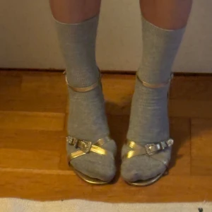 Guldiga sandaler med klack och rosett - Jättefina guldiga sandaler med klack med coolt spänne och omlottband framtill🥰 