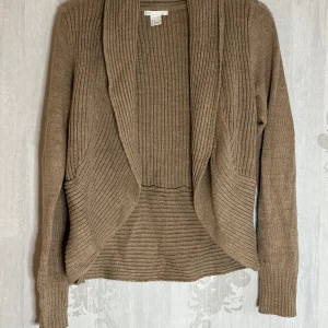 Beige stickad kofta från H&M - Säljer en mysig beige stickad kofta från H&M. Koftan har en öppen design med ribbade detaljer och långa ärmar. Perfekt för kyliga dagar och att slänga över en topp för extra värme. 🧥