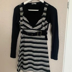 Randig klänning med bälte från Angellila - Snygg klänning från Angellila med svart och vit randigt mönster. Den har långa ärmar och ett coolt bälte i midjan som ger en extra touch. Perfekt för att sticka ut med stil!