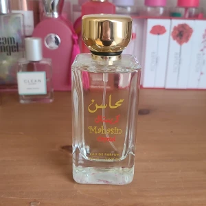 Mahasin Crystal Eau de Parfum - Elegant parfymflaska med gyllene kork och arabiska bokstäver i rött och guld. Flaskan är genomskinlig och stilren, perfekt för den som söker en unik doftupplevelse. Oanvänd. 228kr som ursprungspris. Ingår även spray parfym versionen
