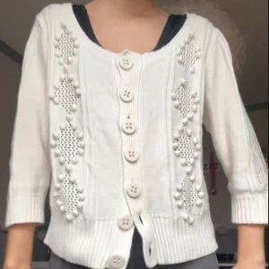 Vit kofta med stora knappar - Säljer en söt vit kofta med stora knappar och dekorativa stickade detaljer💕. Koftan har trekvartsärmar och en ribbad nederkant. Perfekt för en stilren och mysig look.🩷skriv vid frågor/intresse💞(storlek xl passar mig med s/m)