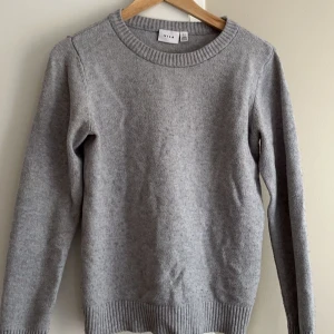 Grå tröja från Vila - Säljer en stilren grå tröja från Vila. Den är långärmad med ribbade kanter vid ärmslut och nederkant. Perfekt för kyligare dagar och enkel att matcha med olika outfits. (EGNA BILDER PRIVAT) 
