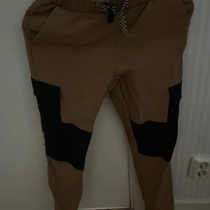 Bruna byxor med svarta detaljer - Snygga bruna byxor med svarta detaljer och snörning i midjan. Perfekta för en avslappnad stil. Byxorna har en bekväm passform och elastisk midja.