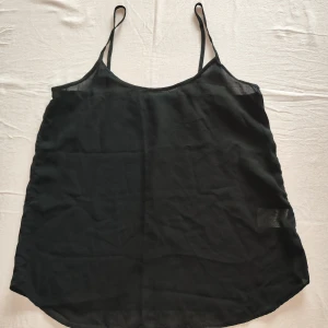 Svart linnetopp från Gina Tricot - Snygg svart linnetopp från Gina Tricot med tunna axelband. Perfekt för varma dagar eller som ett lager under en jacka. Tillverkad i lätt och luftig polyester.