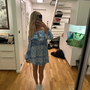 Blå och vit offshoulder klänning från Ivyrevel - Säljer en superfin blå och vit offshoulder klänning från Ivyrevel. Klänningen har ett vackert mönster och volangdetaljer vid ärmarna. Perfekt för sommarens alla tillfällen! 💙