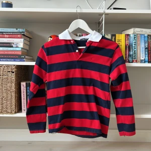 Randig pikétröja från Polo Fashion - Säljer en klassisk randig pikétröja från Polo Fashion i rött och blått. Tröjan har en vit krage och långa ärmar, perfekt för en stilren look. Passar både till vardags och mer avslappnade tillfällen. 🏷️