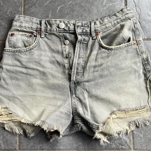 Grå jeansshorts med fransar - Snygga grå jeansshorts med fransiga kanter och knappar framtill. Perfekta för en avslappnad stil. De har klassiska fem fickor och bälteshällor.