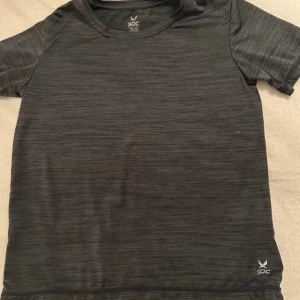 Grå tränings-t-shirt från SOC - Säljer en grå tränings-t-shirt från SOC med teknologin TCS Airflow för optimal ventilation. Perfekt för träning och aktivitet. Kortärmad och tillverkad i ett lätt syntetmaterial för att hålla dig torr och bekväm.