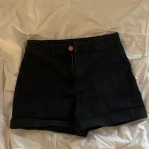 Svarta shorts med uppvikta ben - Snygga svarta shorts med uppvikta ben och klassisk design. De har en knapp och dragkedja framtill samt fickor både fram och bak. Perfekta för en stilren look. Kan justeras vid behov