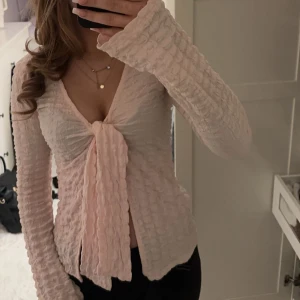 Rosa ribbad knyt topp  - Säljer en söt ljusrosa topp med ribbad textur och knyt framtill. Toppen har långa utsvängda ärmar och en v-ringad design som ger en feminin touch. Nästan aldrig använd
