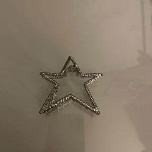 Silverfärgad stjärnformad hårklämma - Snygg stjärnformad hårklämma i silverfärg. Perfekt för att ge en extra touch till din frisyr. Klämman har en öppen design med små detaljer längs kanterna.